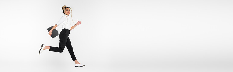 smiling african american businesswoman with paper folder running in air isolated on white, banner