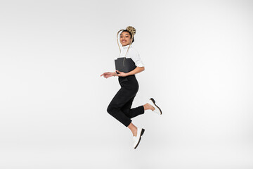 cheerful african american businesswoman looking at camera while levitating with paper folder isolated on white