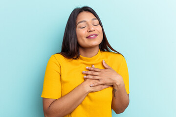 Young Venezuelan woman isolated on blue background has friendly expression, pressing palm to chest. Love concept.