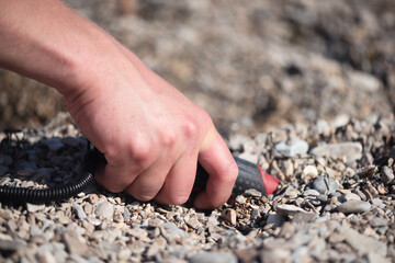 Man with a pin pointer metal detector on the sea beach is looking for the lost coins. Summer hobby.