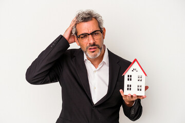 Middle age business man holding bills and house model isolated on blue background  being shocked, she has remembered important meeting.