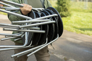 A man carries chairs. Lots of chairs in hand. Furniture on the street.