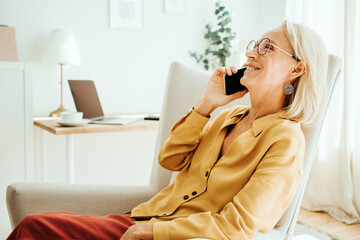 Handsome mid aged woman at her bright and sunny apartment. Mobile phone conversation