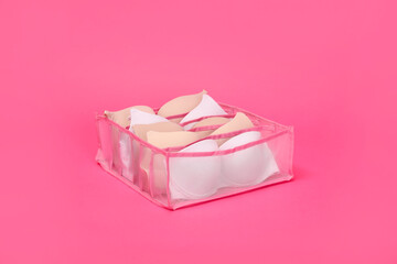 Transparent organizer with bras on pink background