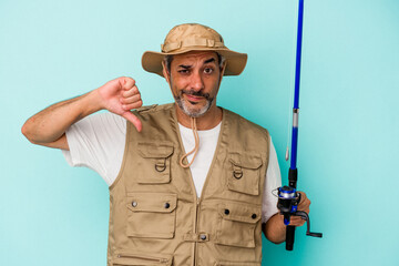 Middle age caucasian fisherman holding rod isolated on blue background  showing a dislike gesture, thumbs down. Disagreement concept.