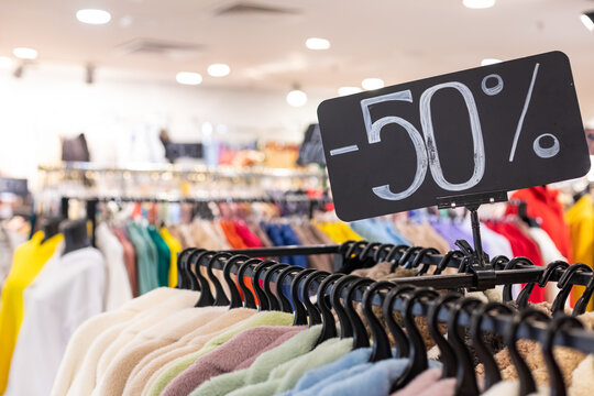 Seasonal sale in the store of women's and men's clothing. Inscription 50 percent discount. Racks with hangers and a collection of clothes. Place for inscription - Powered by Adobe