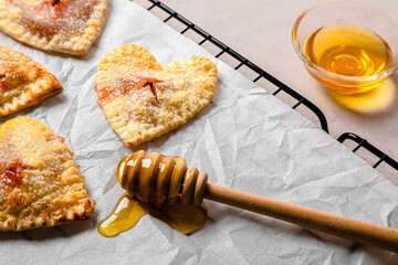 Studio shot of bowl of honey, honey dipper and freshly baked heart shaped mini pies