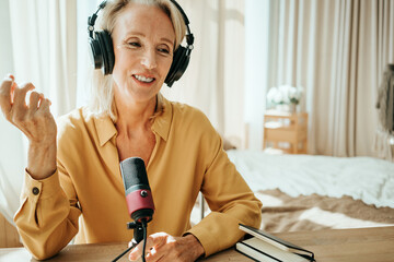 Stylish mature woman at her cozy home apartment. Straming her first audio podcast