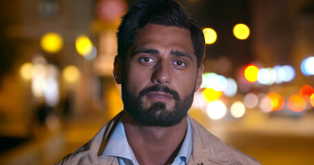 Bokeh shot of handsome indian man looking at camera in city at night