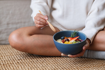 A woman holding and eating healthy blueberry smoothie bowl with mixed fruits topping at home