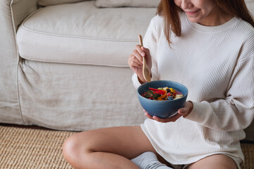 A woman holding and eating healthy blueberry smoothie bowl with mixed fruits topping at home