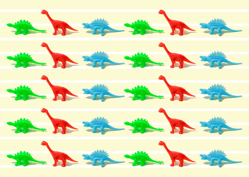Pattern of green, red and blue plastic dinosaur figurines flat laid against yellow background