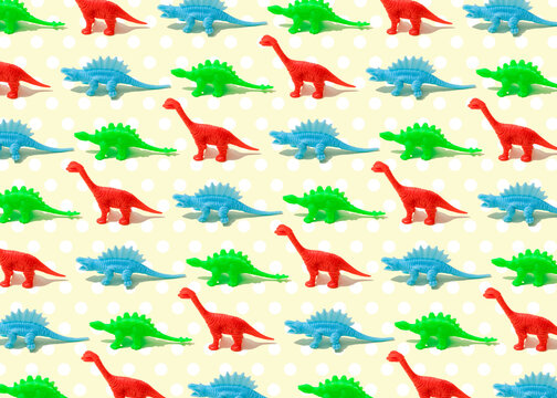 Pattern of green, red and blue plastic dinosaur figurines flat laid against yellow background