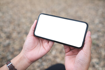 Mockup image of a woman holding mobile phone with blank white desktop screen in the outdoors
