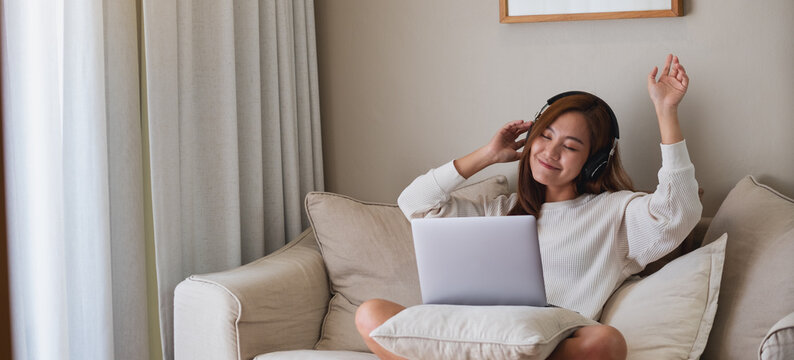 A young woman dancing while enjoy listening to music with headphone and laptop computer at home