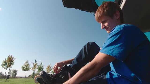 Man putting on roller skates sitting on the car trunk