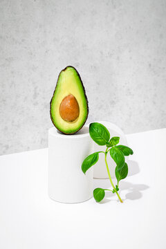 Studio shot of basil leaves leaning on small pedestal with halved avocado