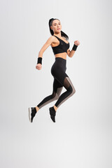 Fototapeta na wymiar full length of young woman in sportswear levitating on grey