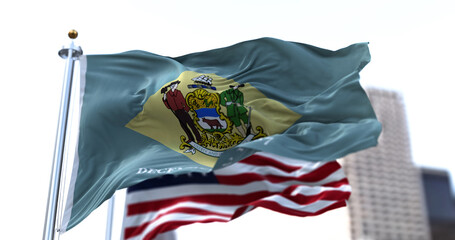 the flag of the US state of Delaware waving in the wind with the American stars and stripes flag blurred in the background - obrazy, fototapety, plakaty