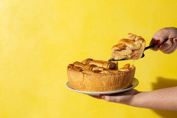 Plate with apple pie in female hands on bright yellow background. Traditional dessert for...