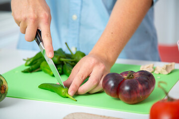 chico joven cortando pimiento verde en una tabla de cortar verde con tomate y manos de chica detras close-up