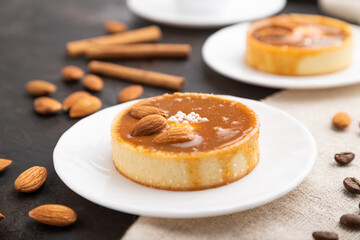 Sweet tartlets with almonds and caramel cream with cup of coffee on a black concrete background. Side view, selective focus.