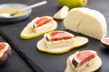 Summer appetizer with pear, cottage cheese, figs and honey on a black concrete background. Side view, selective focus.