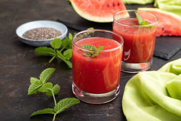 Watermelon juice with chia seeds and mint in glass on a black concrete background with green textile. Side view,  close up.