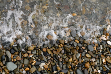 Waves hitting a pebble beach on a summer day. Top view. Background for sea, beach and vacation themes.