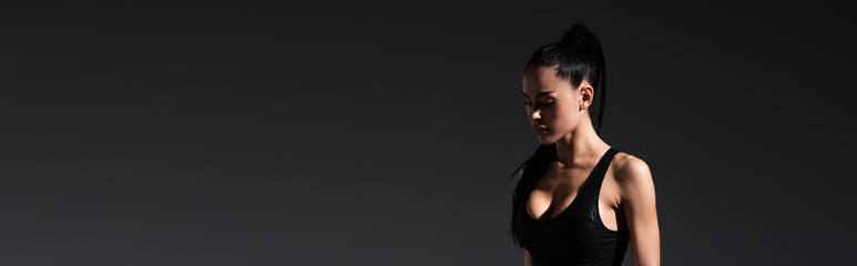 Fototapeta na wymiar young sportswoman in black sportswear standing on dark background, banner