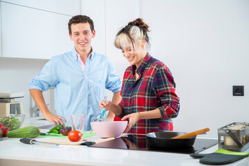 pareja joven sonriente cocinan baten huevos en cocina blanca con verduras, placa de induccion 