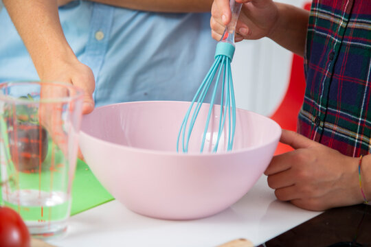 manos de mujer batiendo huevos en un bol rosa utilizando varilla azul en una cocina blanca close-up