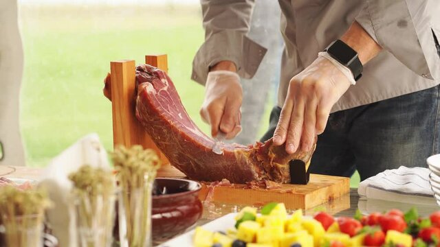 a man in gloves cuts into thin pieces of dried meat for a banquet. 