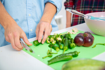 chico joven cortando pimientos verdes en una tabla de cortar verde con tomate sobre una encimera blanca