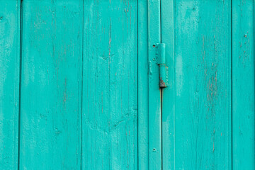 A fragment of an old wooden door of blue or turquoise color on rusty hinges.