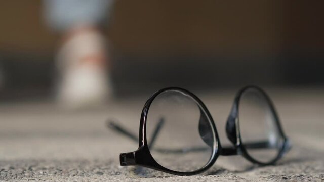 Close-up eyeglasses on the floor with unrecognizable teenagers fighting at background. Feet of angry aggressive Caucasian girls moving as classmates bullying nerd student. Antisocial behavior