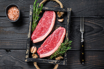 Raw brazilian picanha steak or top sirloin beef meat steak in a wooden tray. Black wooden background. Top view