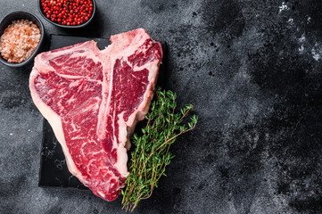 Dry-aged Raw T-bone or porterhouse beef meat Steak with herbs and salt. Black background. Top view....