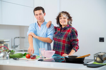 pareja joven sonriente haciendo una masa en un bol rosa, en una cocina blanca con placa de induccion, una sarten de hierro y usan herramientas de madera