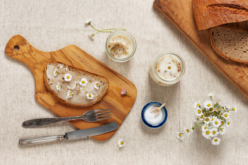 Delicious goose fat with bread and daisy edible flowers served on a wooden cutting board. Top view. © Oksana Schmidt