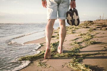 Young man walking barefoot on the beach in sunset time. Nature and travel concept