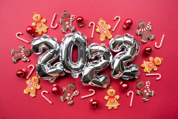Banner. Happy New Year. Silver foil balloons with the number 2022, gingerbread men and Christmas lollipops on a red background. Flat lay. Top view.