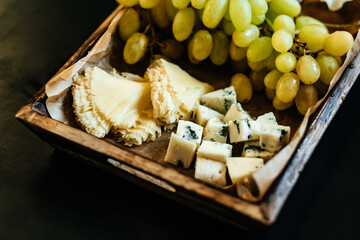 Savory pieces of cheese served with nuts, fruit and honey. Cheese of different varieties on a wooden plate. Dark background.