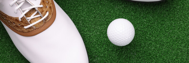 White shoes and ball lying on green golf course closeup
