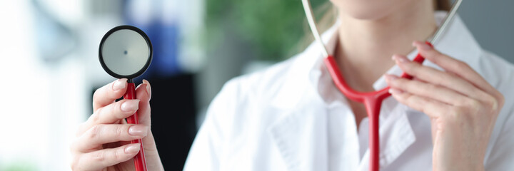 Young woman doctor holding red stethoscope in clinic closeup