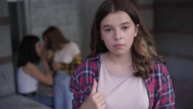 Stressed nervous horrified girl looking back at classmates laughing and looking at camera crying. Portrait of worried desperate bullied student posing outdoors. Bullying and adolescent aggression
