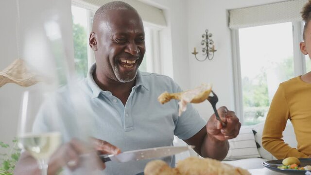 Grandfather carving as multi generation family sit around table at home and enjoy eating meal together - shot in slow motion