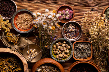 Natural medicine background. Assorted dry herbs in bowls and brass mortar on rustic wooden table.
