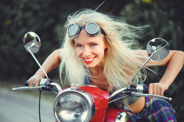 Fototapeta na wymiar The biker is a beautiful cheerful girl sitting on her motorcycle, a little crazy. Wear short shorts and glasses. holding the steering wheel the wind blows the hair. Looks into the distance at the road