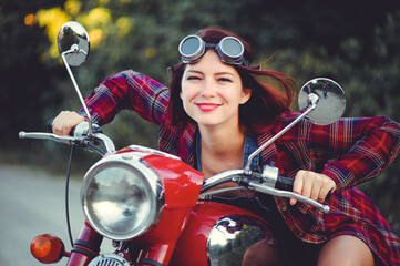 Plakat The biker is a beautiful cheerful girl sitting on her motorcycle, a little crazy. Wear short shorts and glasses. holding the steering wheel the wind blows the hair. Looks into the distance at the road
